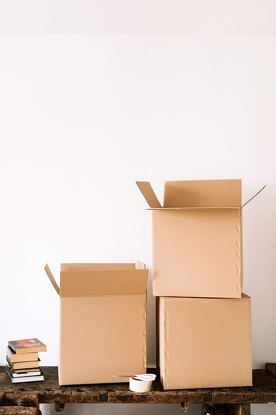 3 brown cardboard boxes atop a shelf with books lying next to them.