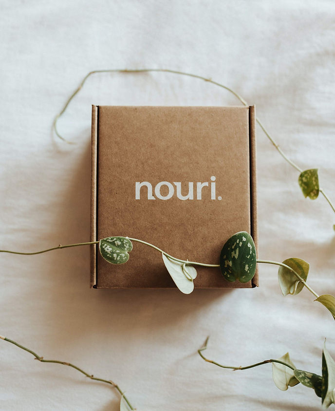 Small, custom brown package with "Nouri" in white letters in the centre. The package is draped over with a stem with a few leaves to add a natural aesthetic.