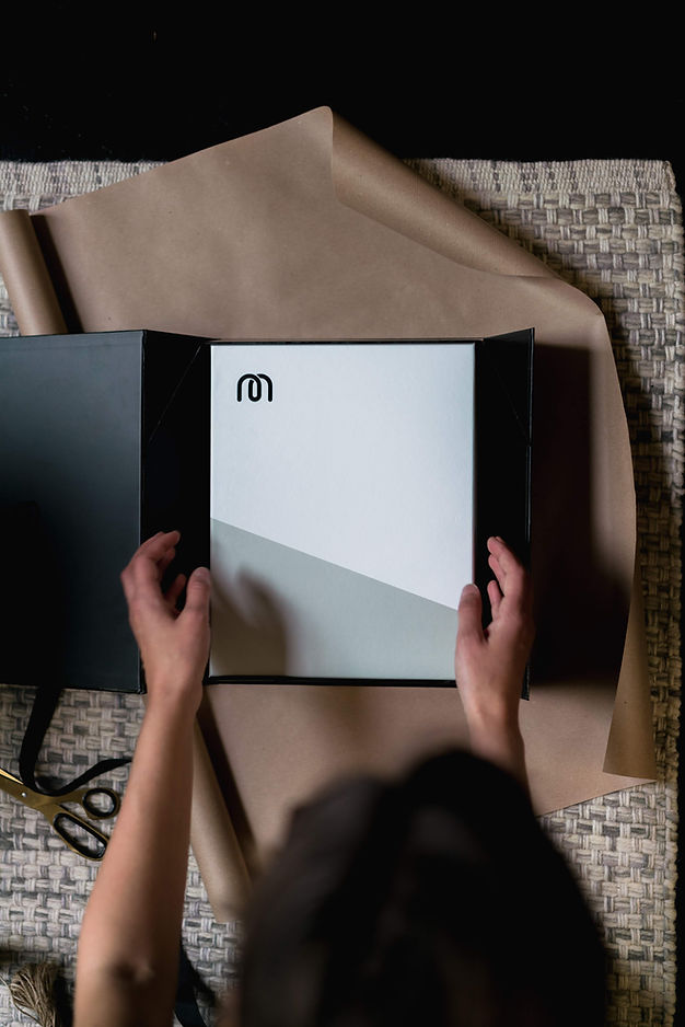 Someone opening a white, branded shipping box with a black "M" company logo at the top left of the box.