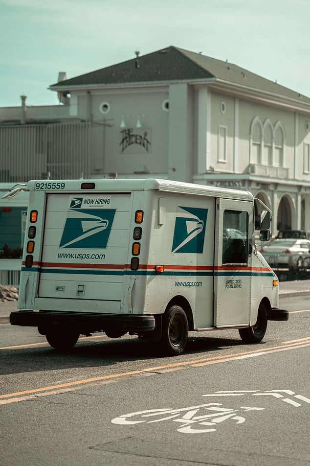 White USPS mail truck driving between Shipping Zones to deliver package.