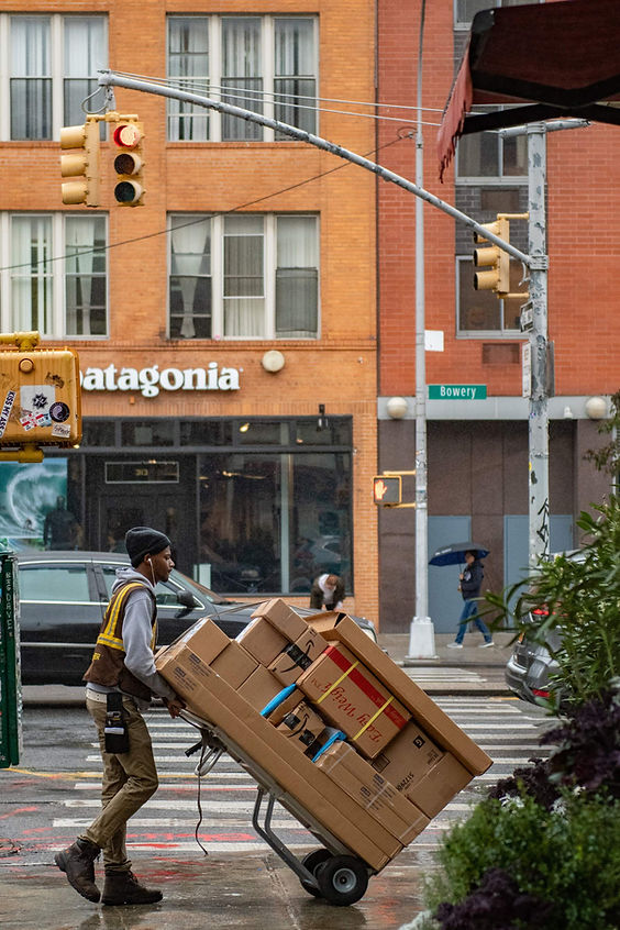 UPS guy pushing a number of large packages next to a busy street. This photo is used to show UPS are the best choice for shipping large packages vs. USPS
