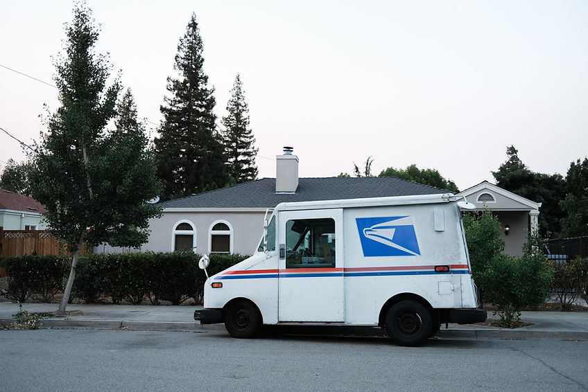 USPS truck in-front of house, with large trees to its left. Photo is being used to illustrate USPS Priority Mail is faster than UPS Ground Service for Small Businesses. 